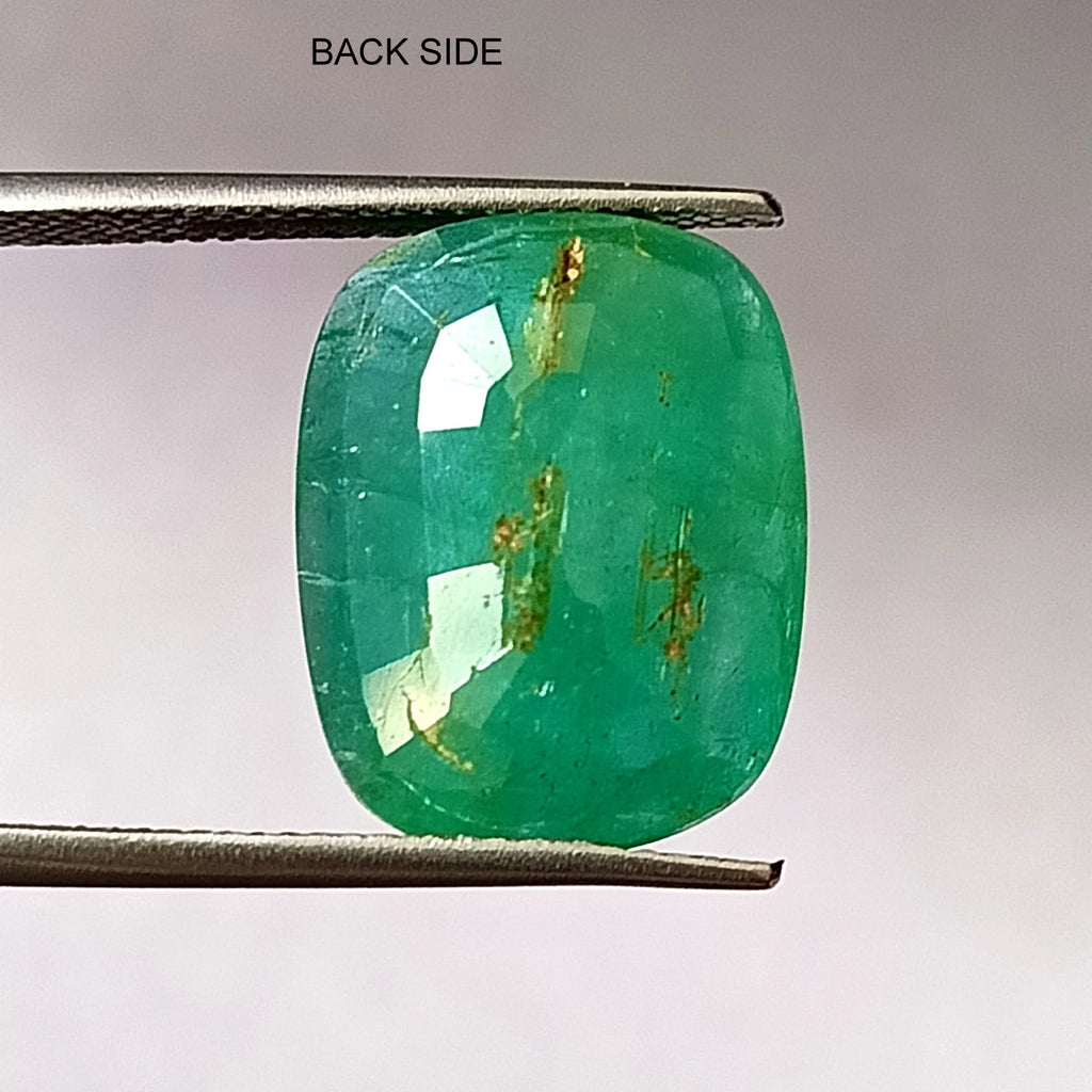 Green oval emerald gemstone back side, faceted, showing internal inclusions in tweezers.