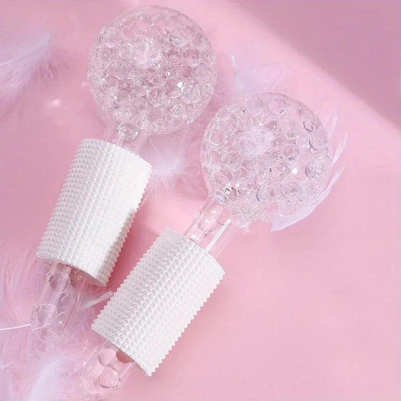 Two clear glass cooling globes for facials with bubble-textured spheres and white textured handles on a pink background.