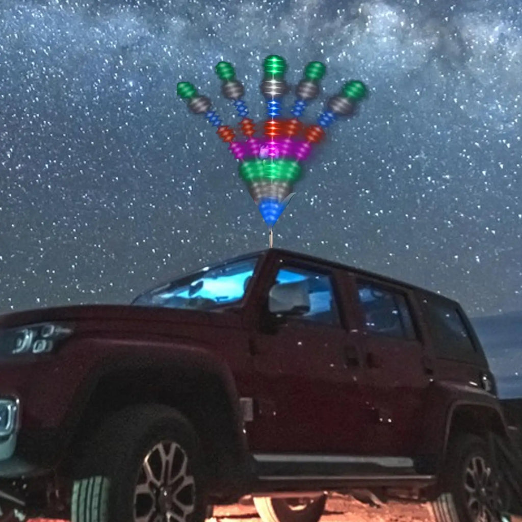 Multi-colored LED wind spinner antenna topper mounted on a car roof against a starry night sky.