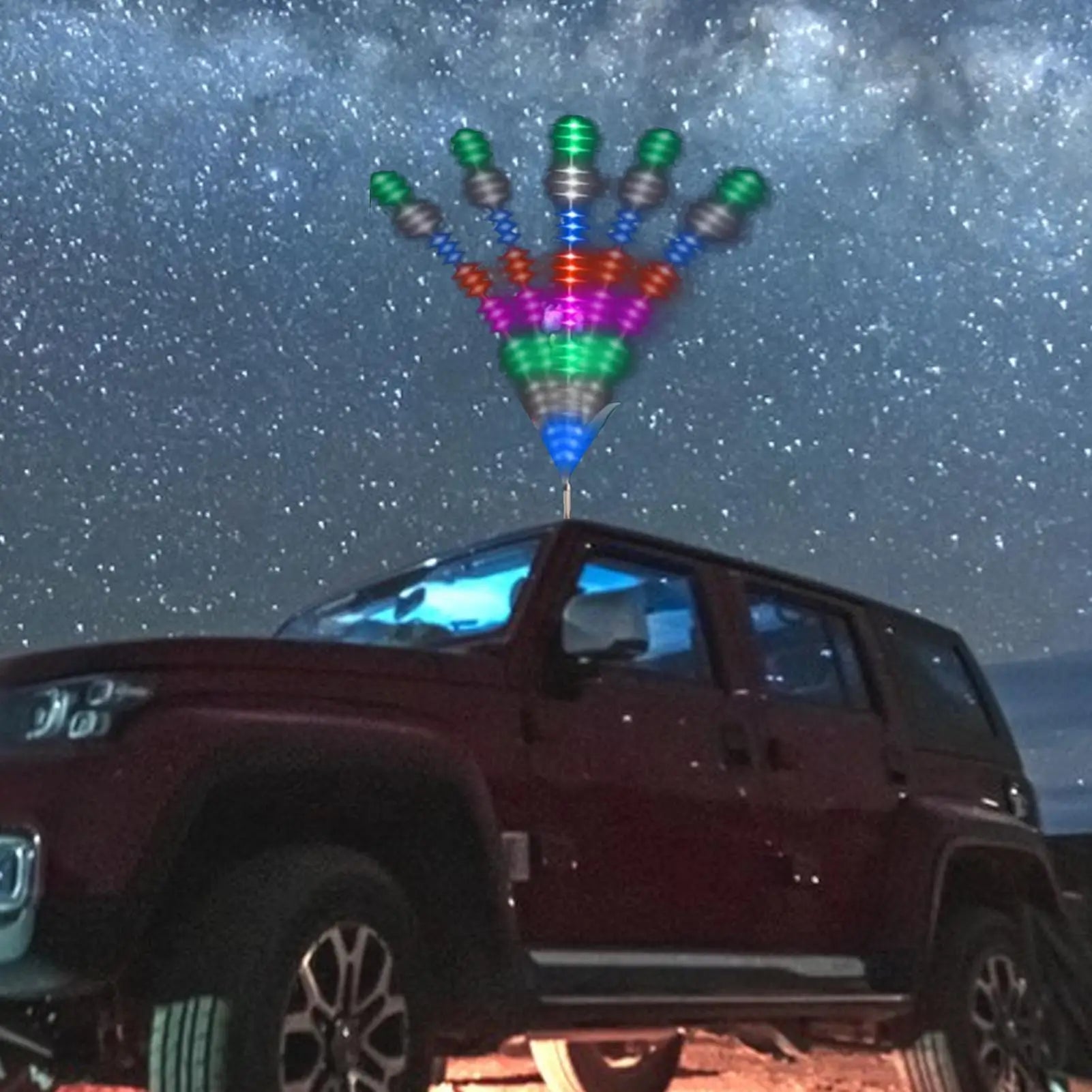 Multi-colored LED wind spinner antenna topper mounted on a car roof against a starry night sky.