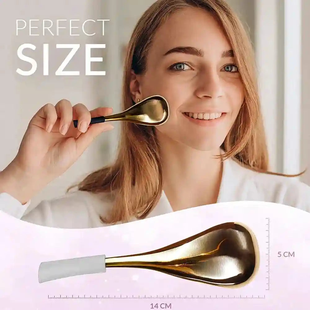 A woman holding a gold, spoon-shaped cooling facial massager. The tool is 14cm long with a 5cm wide metal head.