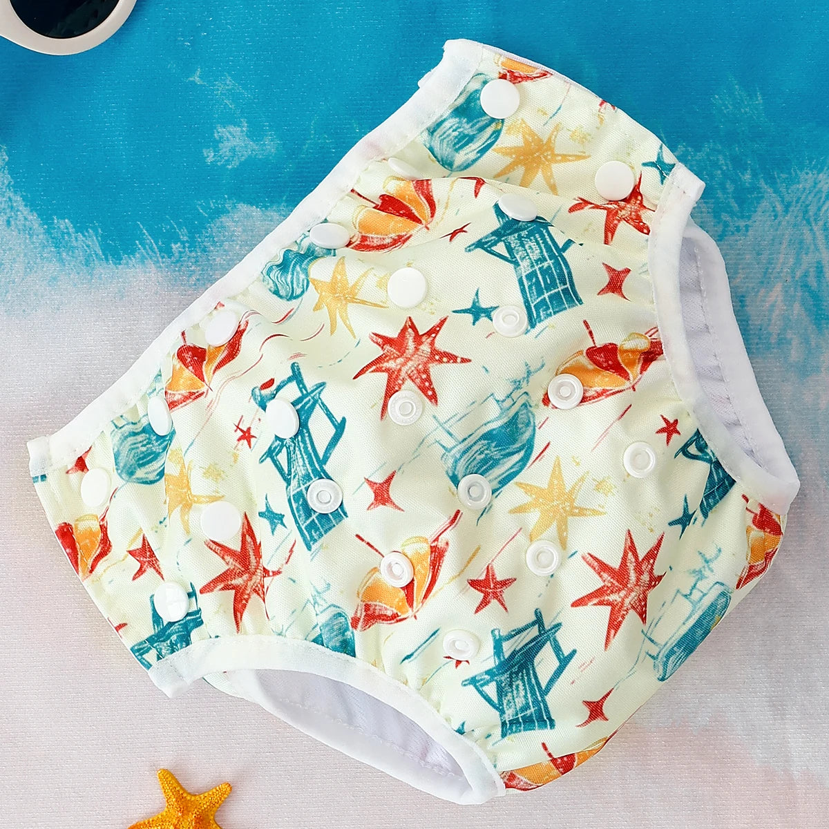 Reusable cloth swim diaper with white snap closures and a colorful nautical starfish and beach chair print.