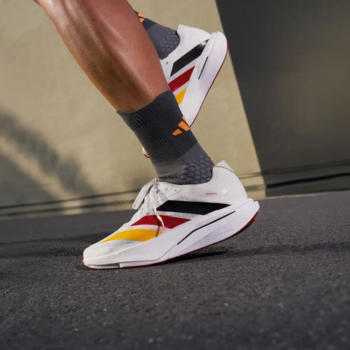 Adidas ZYRION PRO carbon plate running sneakers in white with red and yellow World Cup colorway on asphalt.