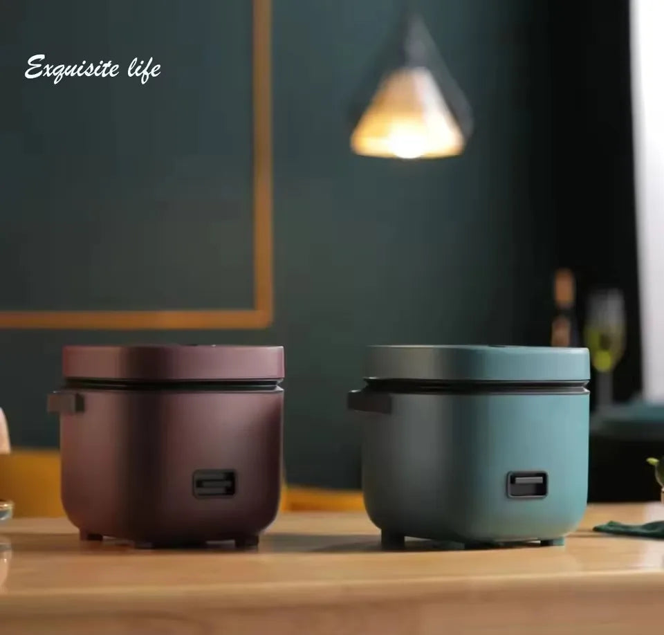 Mini electric rice cooker with dark bronze body and black handles on table.