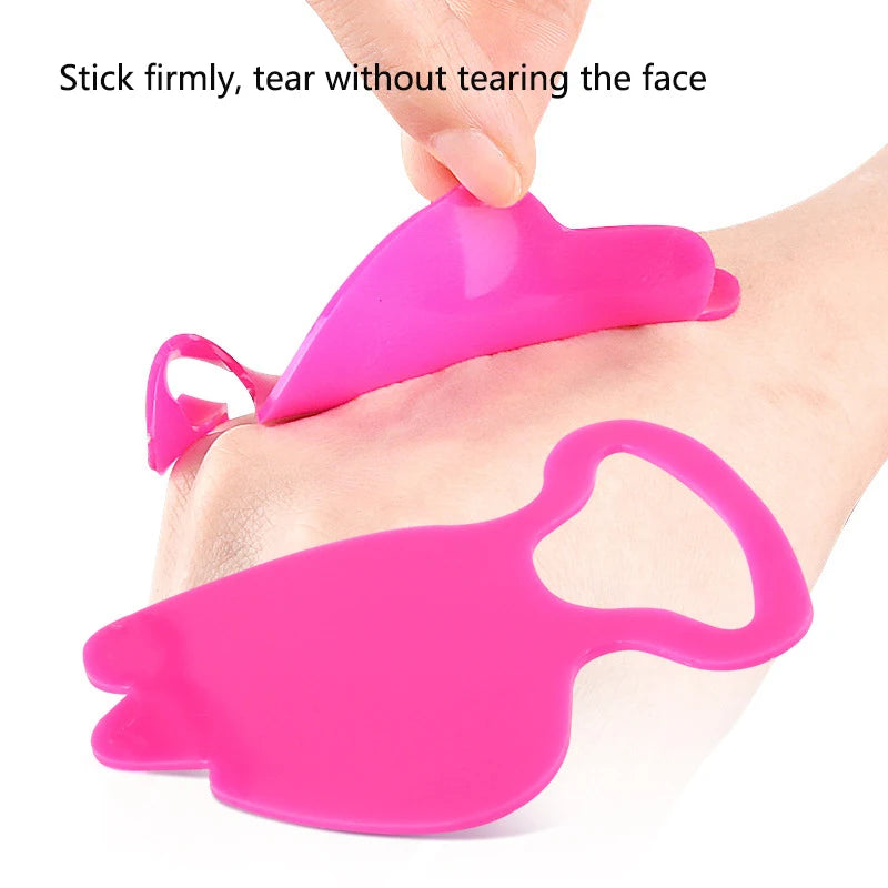 A hand peeling a bright pink, flexible, heart-shaped silicone anti-wrinkle facial patch off the skin.