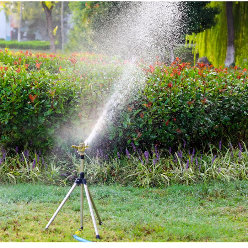 Tripod rotating impact sprinkler with adjustable nozzle, spraying water over garden plants