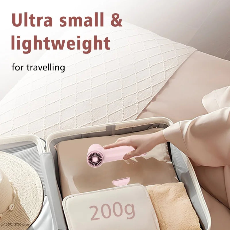 Pink portable mini hair dryer in suitcase. Lightweight 200g high-speed travel hair dryer with nozzle attachment.