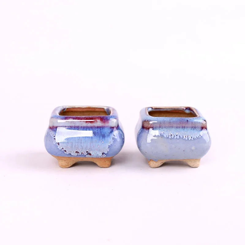 Two mini ceramic succulent pots with blue speckled glaze and small tan pedestal feet