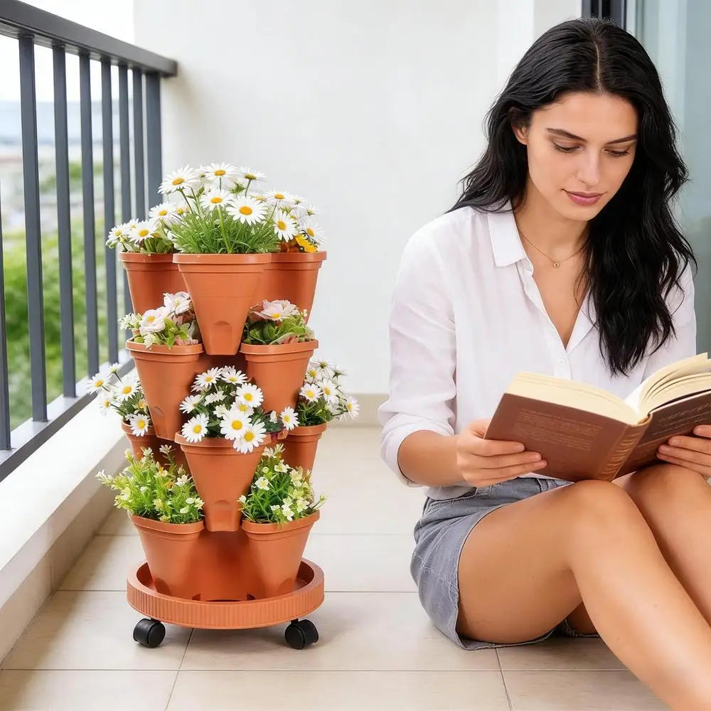 Orange plastic vertical planter tower with stacked pots of white daisies next to a seated reader