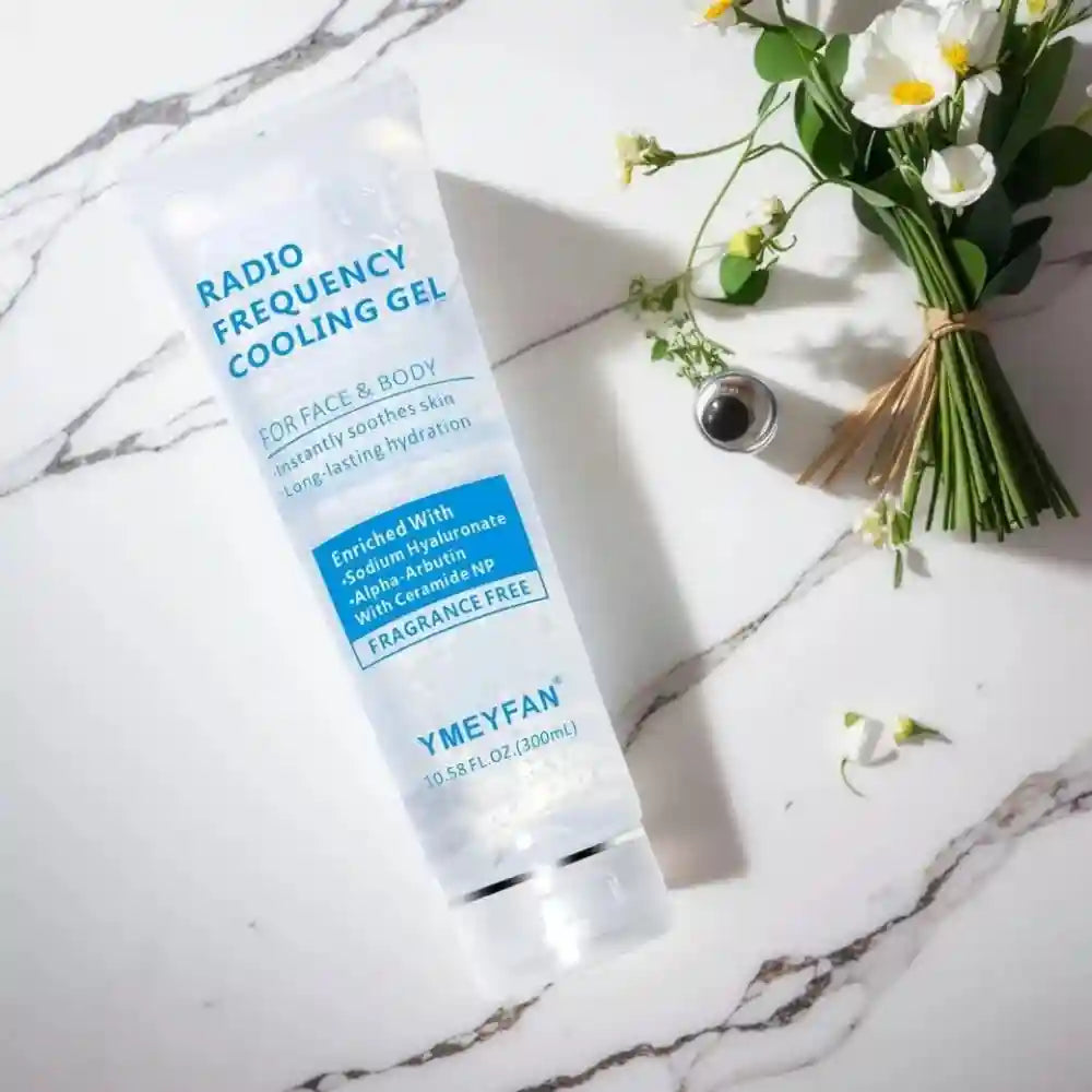 A transparent tube of YMEYFAN conductive gel on a marble surface next to a bouquet of small white flowers.