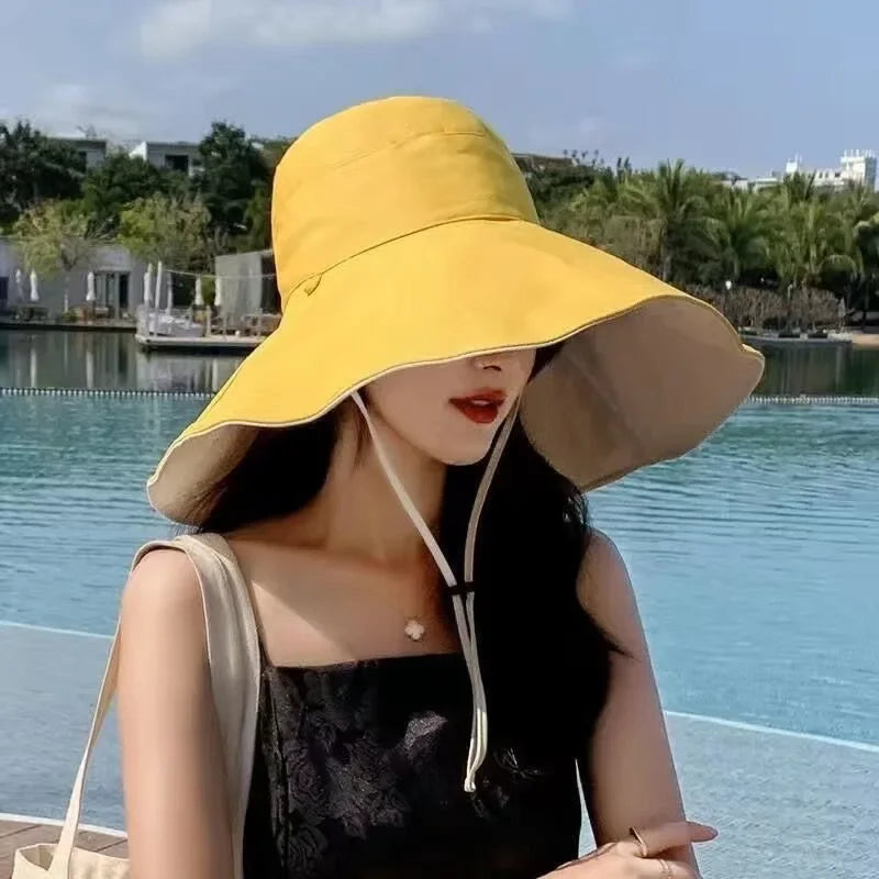 A woman wears a Tidesmit yellow, double-sided wide-brim sun hat with an adjustable chin strap by the water.