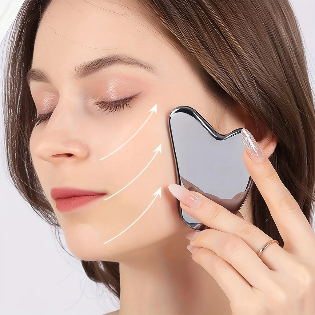 Woman using a silver, dolphin-shaped stainless steel gua sha tool on her cheek with upward motion arrows.