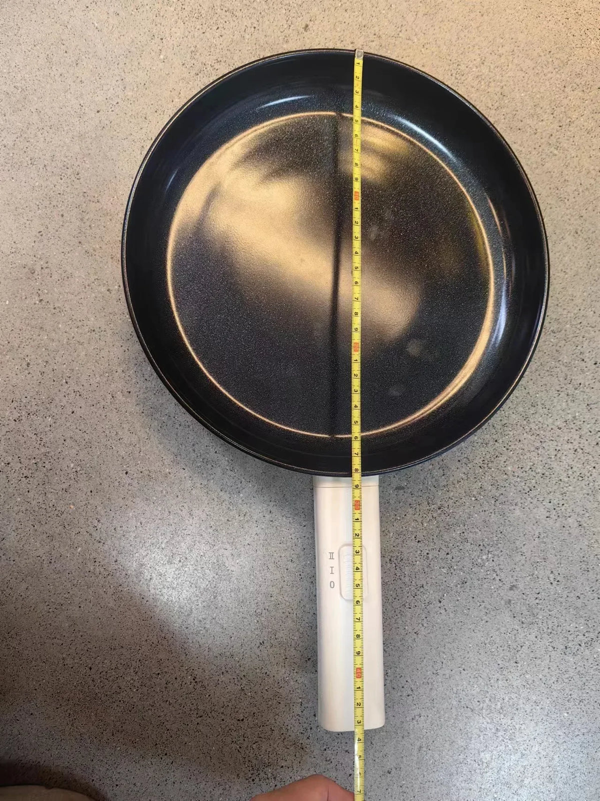 Electric frying pan with black nonstick interior, white rim and handle, measured with ruler