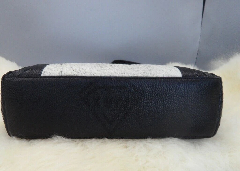 Luxury designer handbag featuring black pebbled leather, woven edges, and a white cowhide fur patchwork panel.