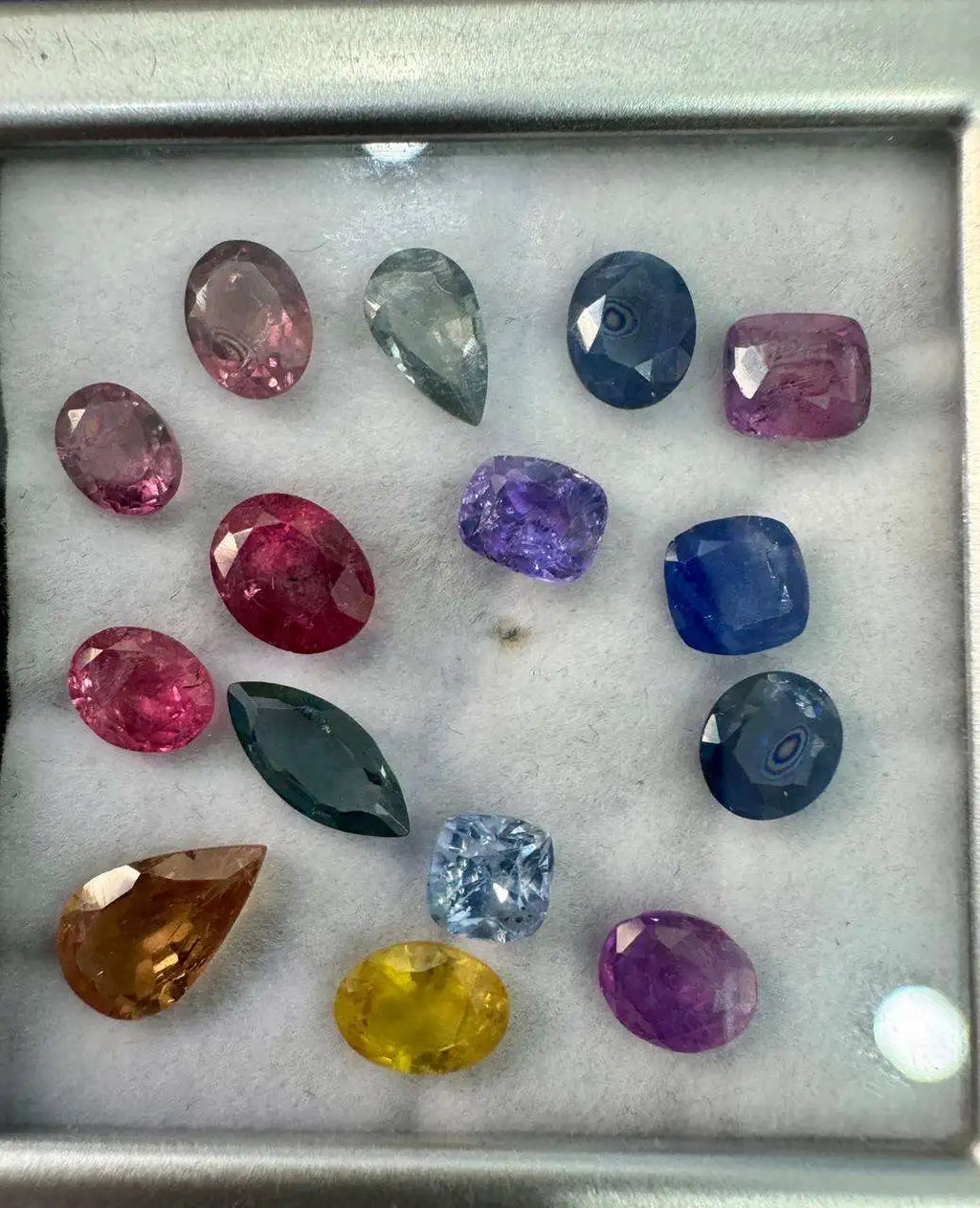 Natural sapphire gemstone mix in metal tray, faceted oval, marquise, and cushion stones