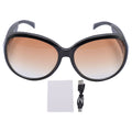 Oversized black smart camera sunglasses with gradient brown lenses, a cleaning cloth, and a USB charging cable.