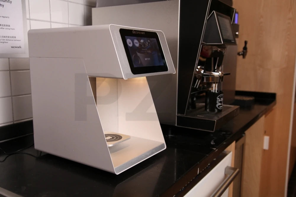 White Ripple Maker coffee printer with touchscreen display for latte art, sitting on a black counter in a WeWork.