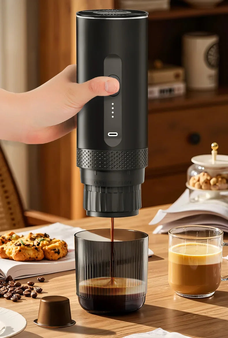 Handheld black portable coffee maker brewing espresso into a glass cup on a wooden table.