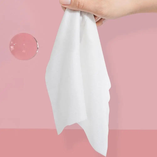 Hand holding a soft, white baby care wipe against a pink background, ideal for sensitive skin and gentle cleaning.