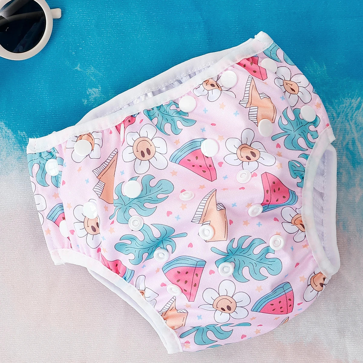Reusable baby cloth diaper in pink with smiley flower, watermelon, and tropical leaf print with adjustable snap closures.