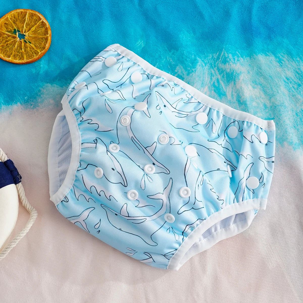 Reusable baby swim diaper in blue with shark pattern and adjustable white snap buttons.