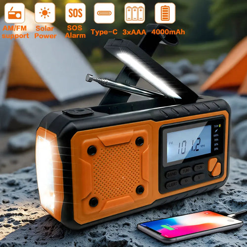 Black and orange solar emergency radio with an LED reading light, flashlight, antenna, and phone charging cable outdoors.