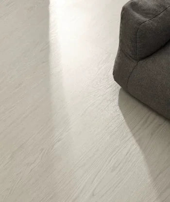 SPC click flooring plank close-up with light wood grain beside a gray sofa