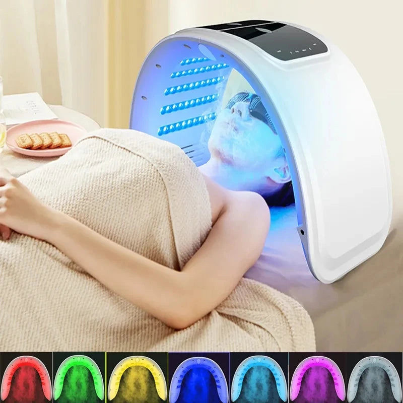 Person receiving blue LED facial light therapy under a white, arched PDT skin rejuvenation device in a spa setting.