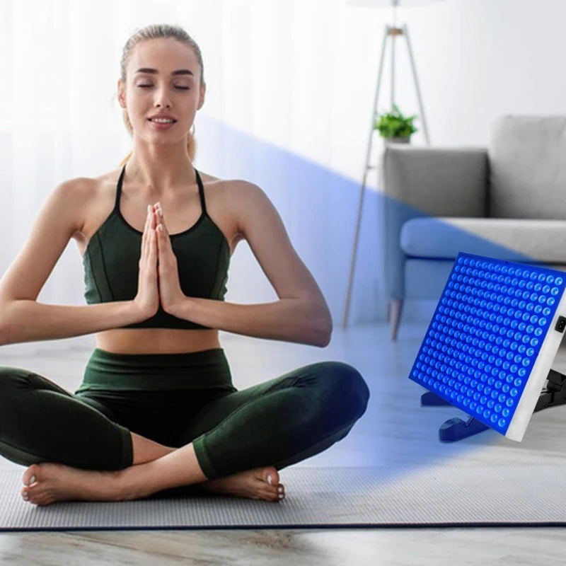 Square blue light therapy panel on a stand, positioned next to a person meditating on a yoga mat.