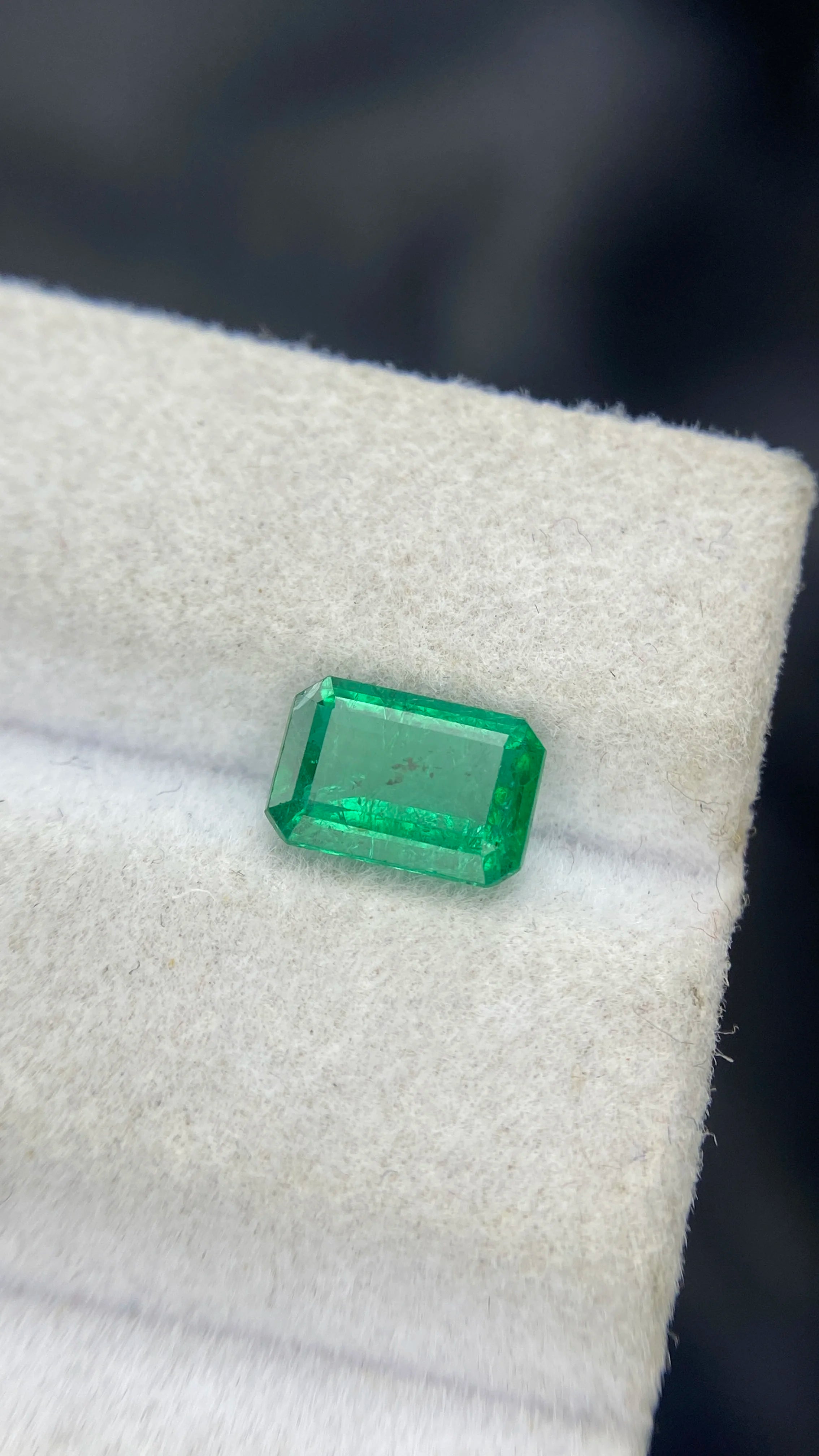 Green emerald-cut gemstone, loose rectangular stone on white display surface