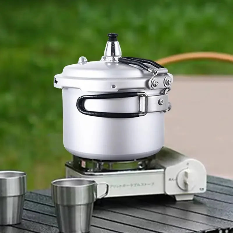 Compact pressure cooker with silver lid and black latch handle on a stove base