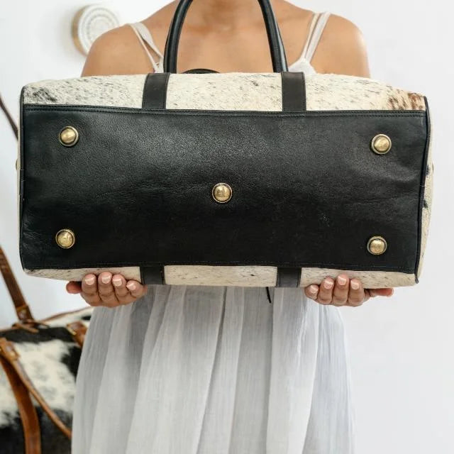 Unisex weekender duffel bag in white cow hair-on-hide with black genuine leather trim and brass protective base studs.