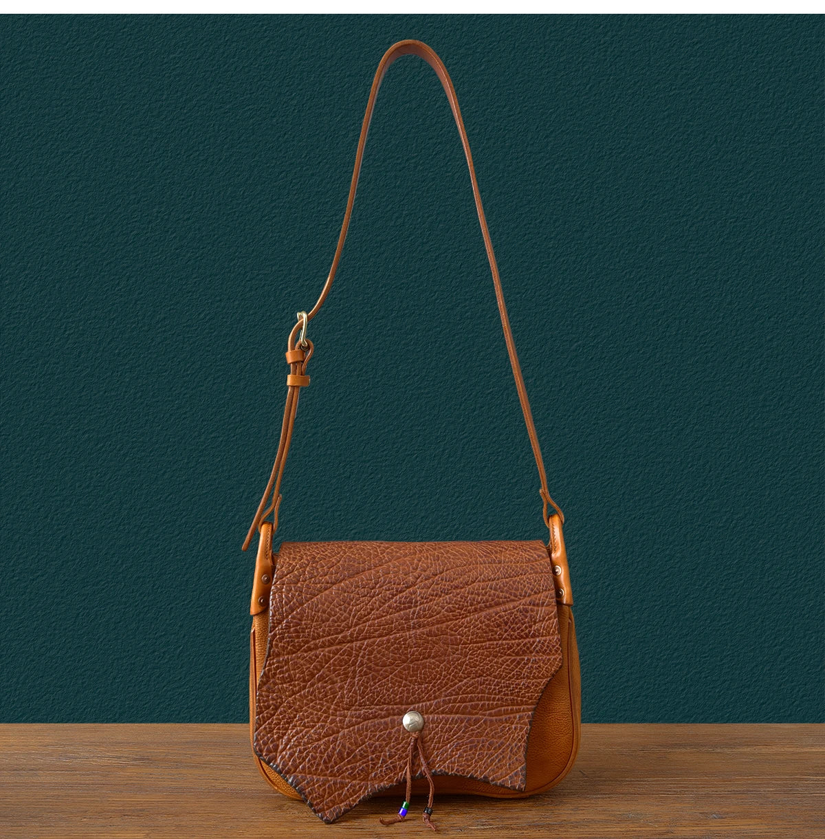 Vintage handmade brown cowhide leather messenger bag with textured flap, adjustable strap, and unique tie closure.