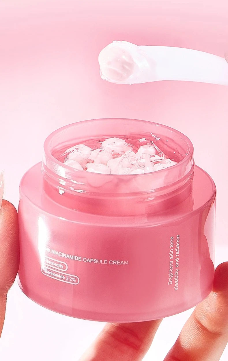 Open jar of pink Niacinamide capsule face cream with a white spatula holding a dollop of product.