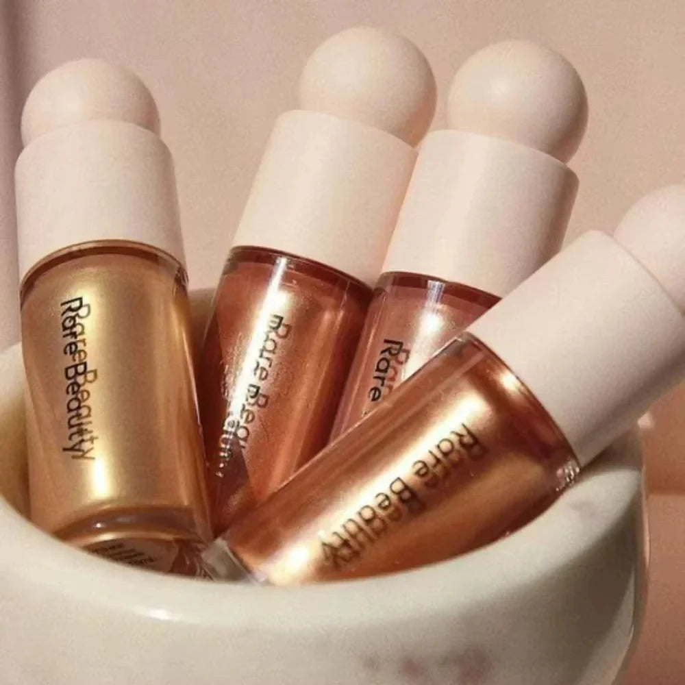 Rare Beauty liquid highlighters in a cluster, showcasing shimmering metallic gold and bronze textures in glass bottles.