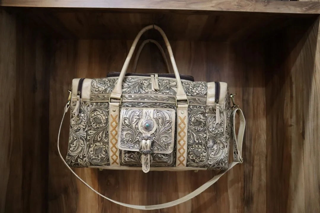 Vintage brown cowhide travel duffel bag with intricate floral tooling, turquoise accent, and handmade western style.