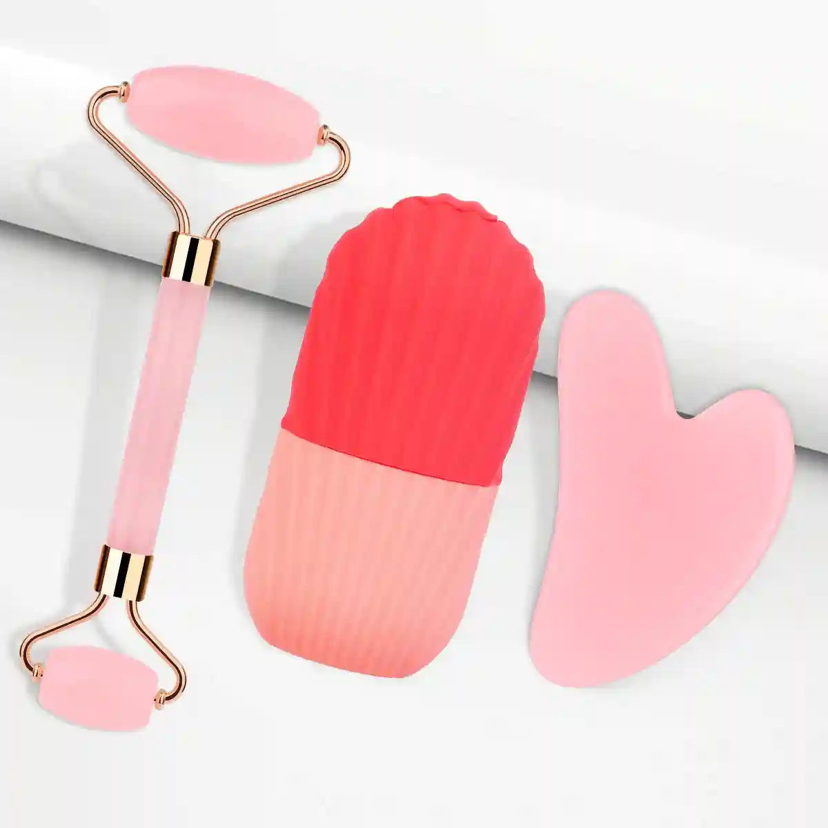 Three-piece facial tool set: rose gold jade roller, red/pink silicone ice roller, and a heart-shaped pink gua sha stone.