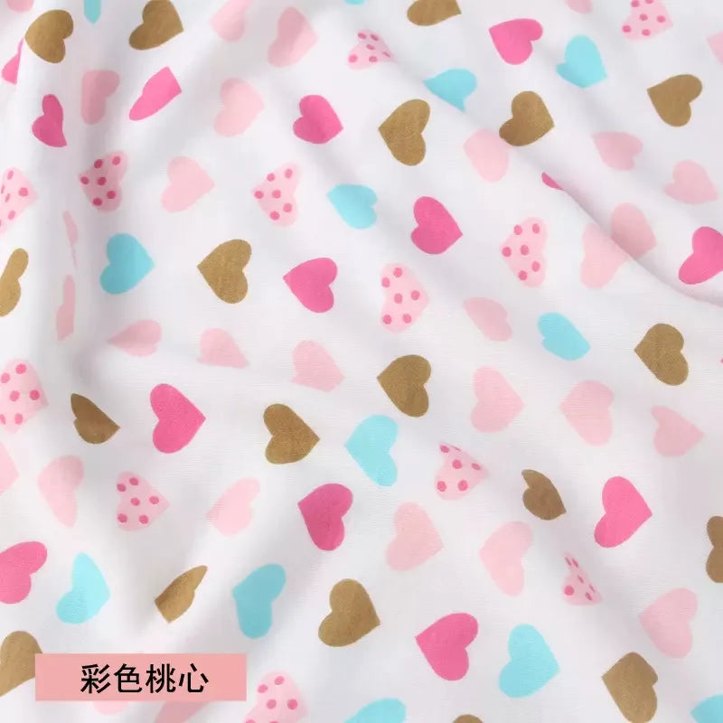 White jersey knit fabric featuring a repeating pattern of pink, blue, and gold hearts, including some polka-dot hearts.