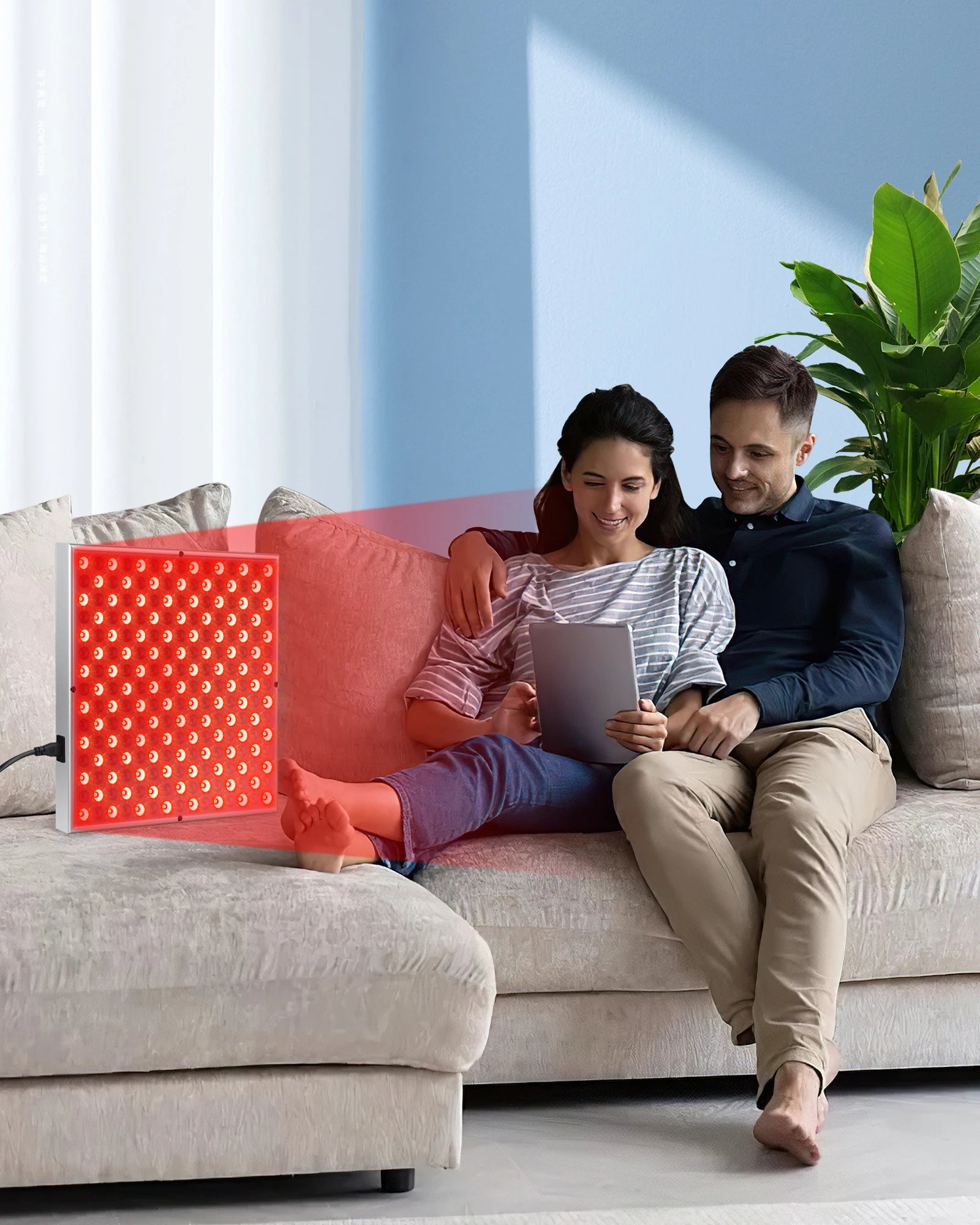 Square LED red light therapy panel on a couch, casting a red glow over a couple relaxing together.