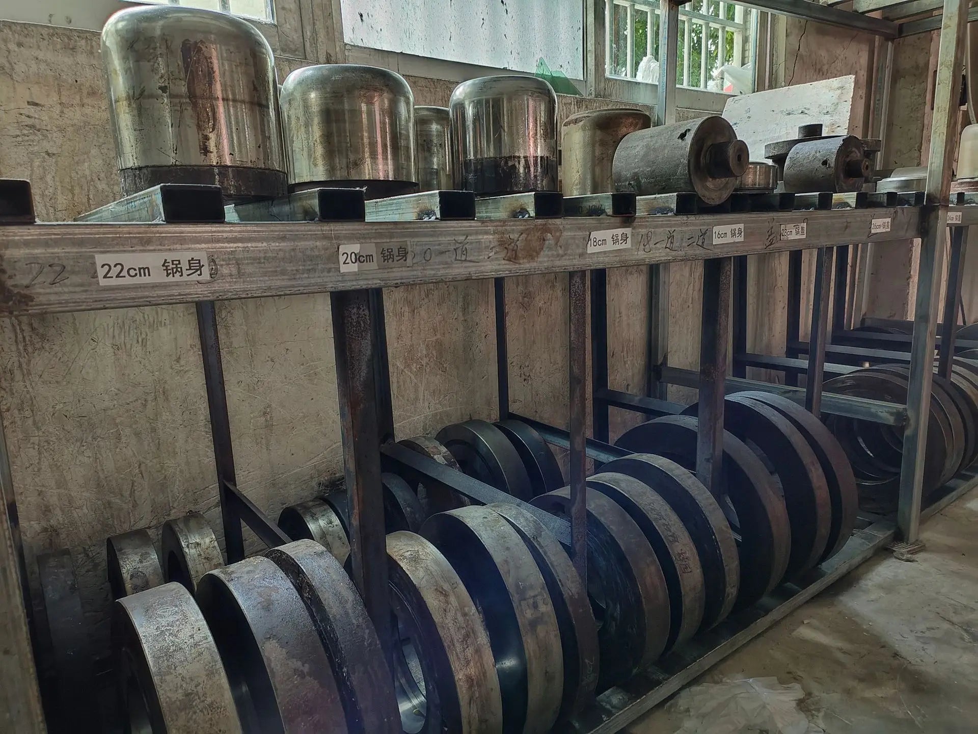 Stainless steel cooker components stored on racks, arranged in multiple rows