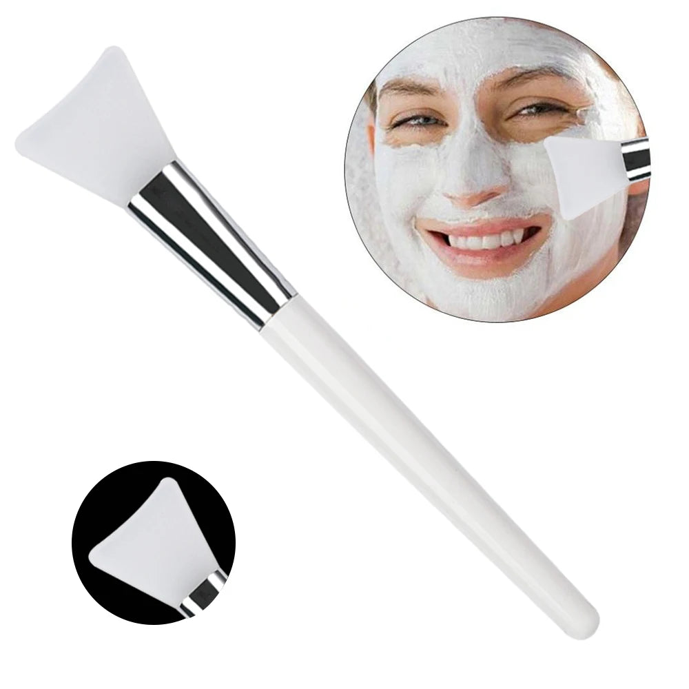 White silicone face mask applicator brush with silver ferrule and white handle, shown applying mask to a woman's face.