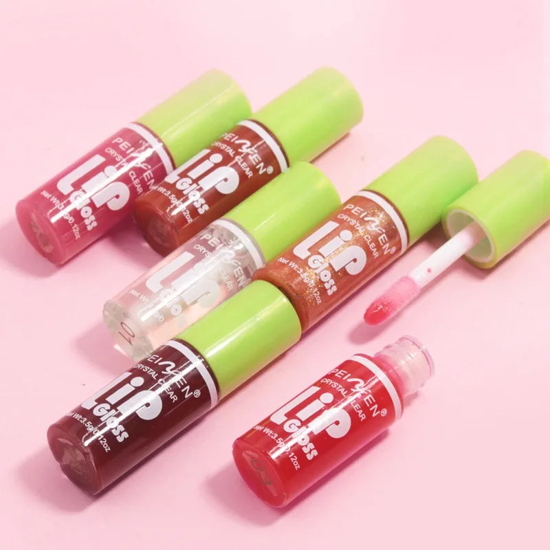Set of 6 moisturizing, high-shine transparent lip gloss oils with green caps on a pink background.