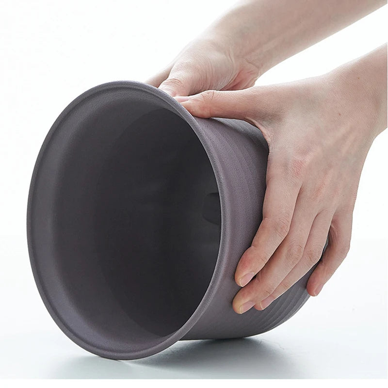 Hand holding a dark gray plastic flower pot insert, open top view