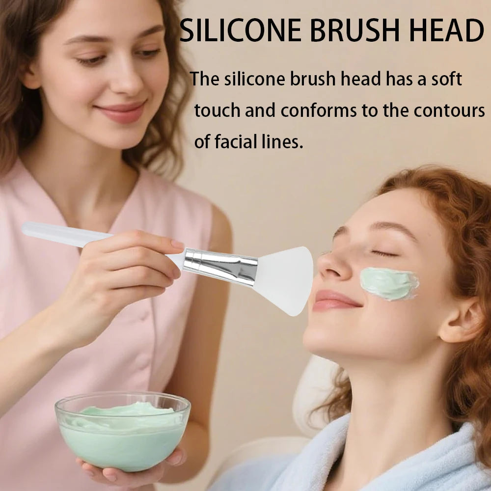 Woman using a white, flexible silicone brush to apply green face mask to another woman’s cheek from a glass bowl.