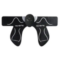 Black, butterfly-shaped EMS hip pad with textured silicone surface and a central electronic control unit for toning.