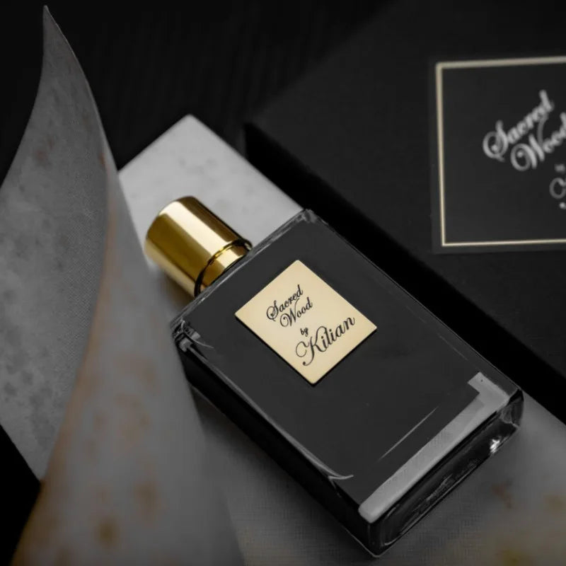 Kilian Sacred Wood unisex perfume: 50ml glass bottle with black liquid, gold cap, and elegant gold label on white stone.