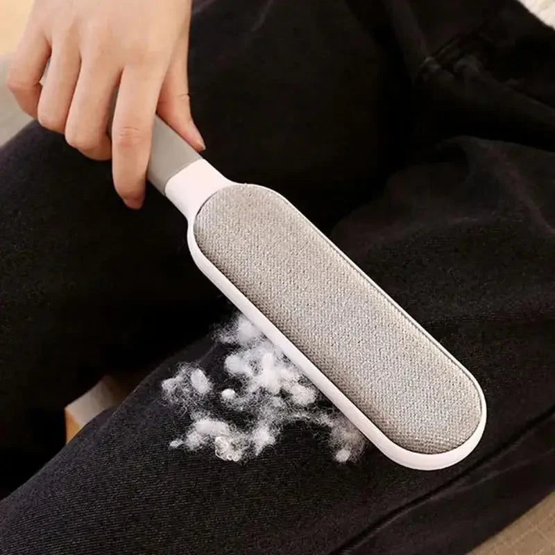 Reusable gray double-sided pet hair remover brush cleaning lint from black pants, sofas, and upholstery.