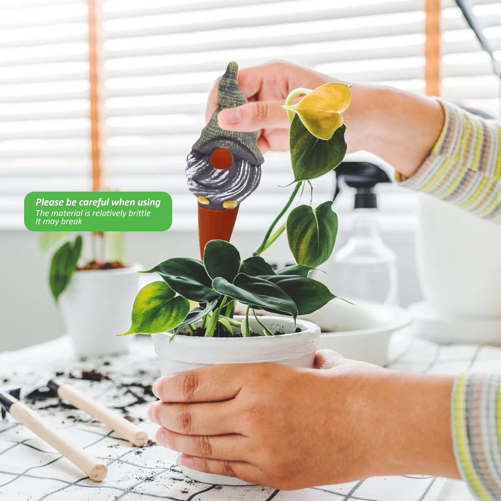 Hands inserting a self-watering globe spike into an indoor plant pot