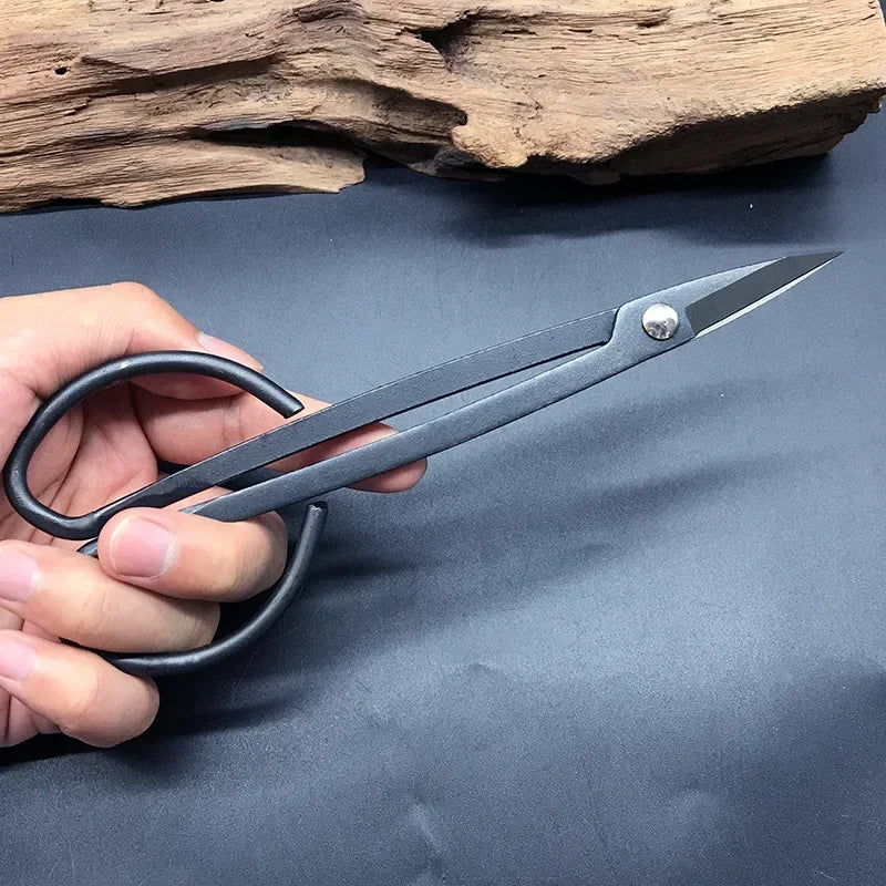 Bonsai pruning scissors held in hand, two steel blades with black loop grips