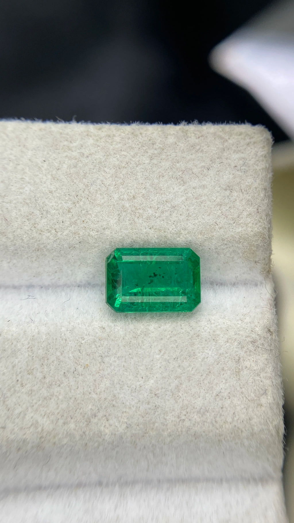 Green emerald-cut gemstone with long rectangular shape, loose stone on white padding